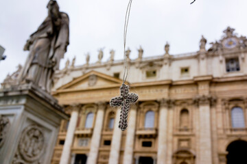 Fototapeta na wymiar A knitted cross hangs in the sky before historic buildings in Vatican City.