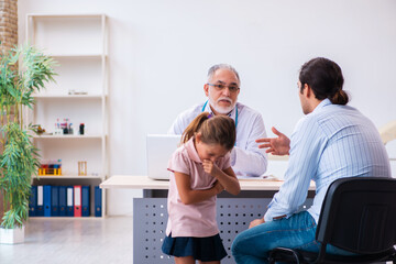 Small girl with her father visiting old male doctor