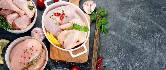 Raw chicken meat parts with spices and herbs for cooking on dark background.