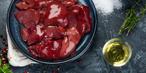 Raw uncooked liver with spices and herbs prepared for cooking on gray background.