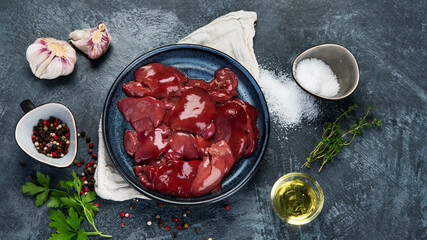 Raw uncooked liver with spices and herbs prepared for cooking on gray background.