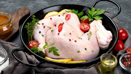 Raw chicken legs with spices and herbs for cooking on gray background.