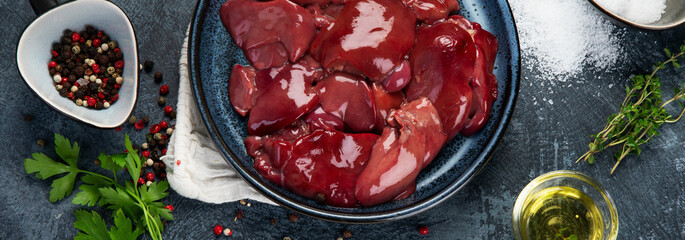 Raw uncooked liver with spices and herbs prepared for cooking on gray background.
