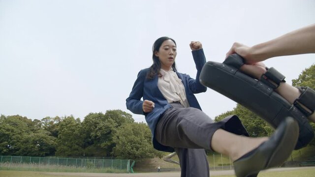Young business woman kicking a boxing pad consecutively, shot from a low angle.