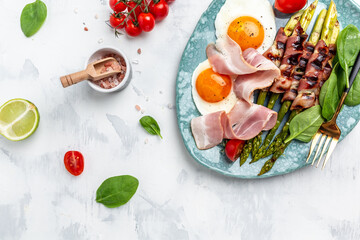 Breakfast fried eggs, asparagus wrapped in bacon, ham, tomatoes and salad. Healthy balanced food. Top view, above, banner
