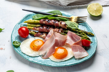Ketogenic diet. Keto brunch breakfast. fried eggs, asparagus wrapped in bacon, ham, tomatoes and salad. Food recipe background. Close up