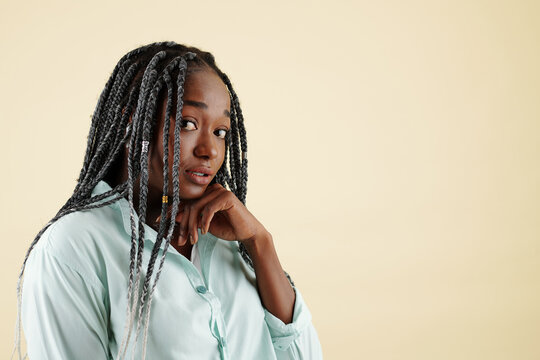 Portrait of shy attractive young woman with braided hairstyle looking at camera, isolated on yellow