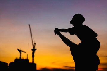 The silhouette of the happy father and son wearing a construction helmet holding hands expressing...
