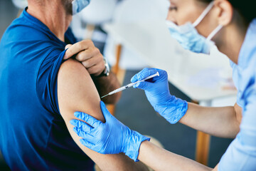 Close-up of nurse vaccinating a man against coronavirus at medical clinic. - obrazy, fototapety, plakaty
