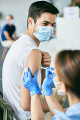 Young man getting vaccinated against COVID-19 at vaccination center. - obrazy, fototapety, plakaty