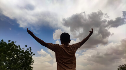 A boy hands up and looking at clouds in the sky