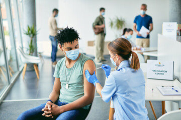 Young African American man getting vaccinated against coronavirus at vaccination center. - obrazy, fototapety, plakaty