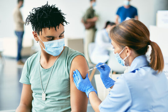 Young black man receiving COVID-19 vaccine during immunization at vaccination center.