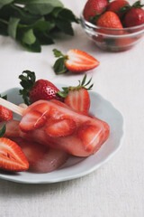 Homemade popsicle with strawberry on kitchen table. Refreshing summer dessert with berry and infused water. Close up, vertical