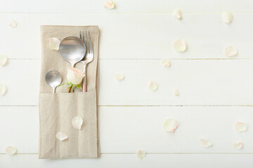Holder with cutlery and flower on white wooden background