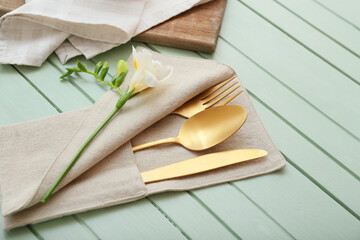 Holder with cutlery and flower on color wooden background, closeup