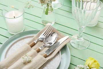 Beautiful table setting with burning candle and flowers on color wooden background, closeup
