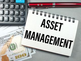 Naklejka premium Business concept.Text ASSET MANAGEMENT with pen,banknote and calculator on gray background.