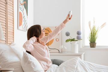 Young woman with air conditioner remote control in bedroom