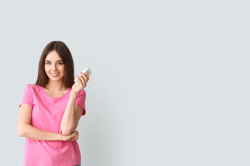 Young woman with air conditioner remote control on light background