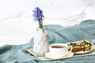 Tray with hyacinth flower and tasty breakfast on bed