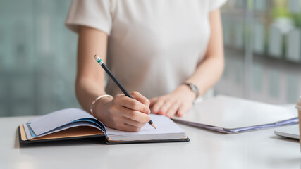 Image of a woman holding a pencil taking notes on the blank paper in the office.