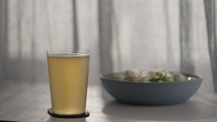 ginger beer in tumbler glass with salad in bowl on white oak table with sunset light