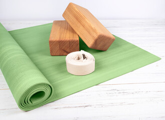 Green yoga mat, two wooden blocks and white belt on white wooden  background. Yoga practice,...