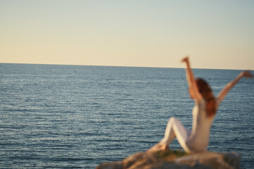 a woman in trousers and a T-shirt sits on the Big Stone near the sea with her hands up