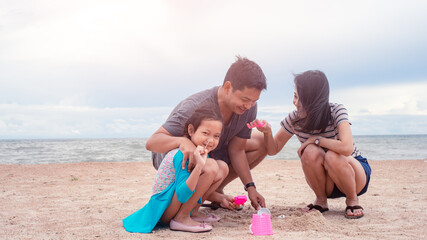 Fototapeta premium Happy Father, mother and daughter are making sand piles on the beach