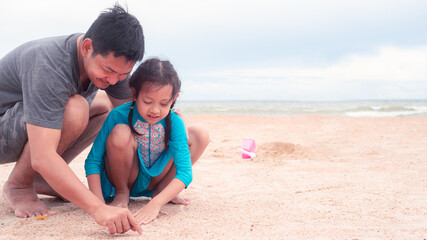 Fototapeta premium Happy father and daughter are making sand piles on the beach.Concept of fathers day