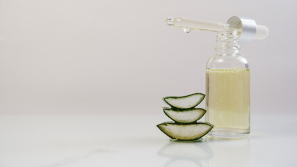 Aloe vera gel bottle with open dropper with sliced aloe vera leaf on white, gray background. Skin care, health, beauty and spa concept.