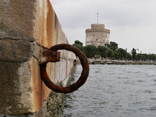 An old rusty metal mooring ring on the mooring wall on a sunny summer day. A device for holding sea vessels in port. heavily rusted iron mooring ring with the harbor in the background.