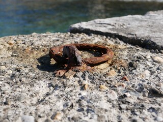 An old rusty metal mooring ring on the mooring wall on a sunny summer day. A device for holding sea vessels in port. heavily rusted iron mooring ring with the harbor in the background.