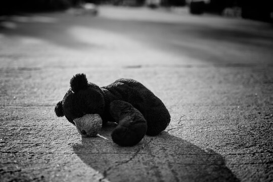 Black and white of alone Toy Teddy bear doll sleep on middle of road. lonely, sad, broken heart or international missing children's day concept.