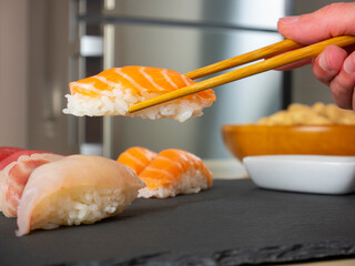 Eating nigiri sushi mix. Hands with chopsticks hold a salmon nigiri. Japanese food. Rice covered with slices of fish.
