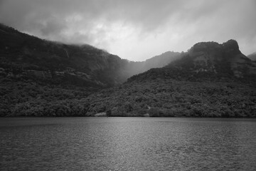 Black and white breadth taking mountain ranges covered with forest surrounded by lake during monsoon season sky covered with clouds in vacation holiday trek at India