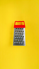 Manual kitchen grater with red handle on yellow background. Copy the space for the text. Kitchen set. Cooking concept. Concepts about homework. Background for food recipes. Vertical photo.