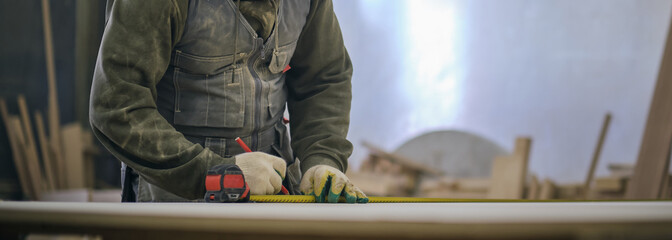 Close up. Carpenter holding a measure tape on the work bench. Woodwork and furniture making concept. Carpenter in the workshop marks out and assembles parts of the furniture cabinet