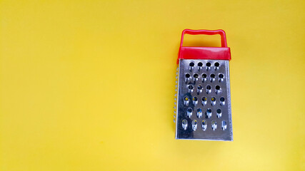 Manual kitchen grater with red handle on yellow background. Copy the space for the text. Kitchen set. Cooking concept. Concepts about homework. Background for food recipes.