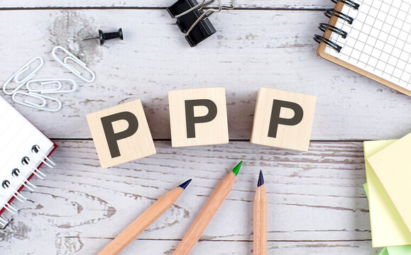 PPP text on wooden block with office tools on the wooden background