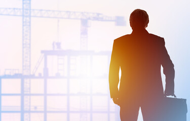 Construction business. Investment in real estate. Silhouette of a man in a business suit on the background of construction. A businessman on the background of houses under construction and cranes.