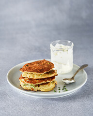 Vegetable zucchini fritters in stack with sour cream and chive, light background, copy space. Healthy clean vegetarian food.