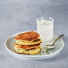 Vegetable zucchini fritters in stack with sour cream and chive, light background, copy space. Healthy clean vegetarian food.