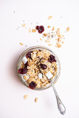 Homemade cereal granola in glass jar. Muesli with oats, nuts, chia seeds, pieces of coconut and dry berries on a light table. Modern concept of healthy eating and sustainable lifestyle.