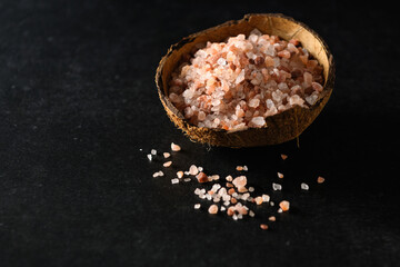 pink himalayan coarse salt in a coconut bowl on dark gray background, empty space for text