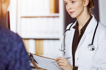Cheerful smiling female doctor and patient woman discussing current health examination while...