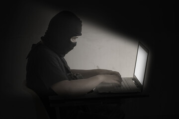 Hacker in black mask using laptop for crime cyber attack network security and stealing personal data infomation.