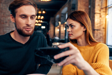 a woman in a sweater with a mobile phone and a guy with a beard are sitting in a restaurant