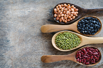 Four kinds of natural cereal and grain seeds consisted of black and red bean, mung, and peanut in wooden spoon on grunge background with copy space for adding text